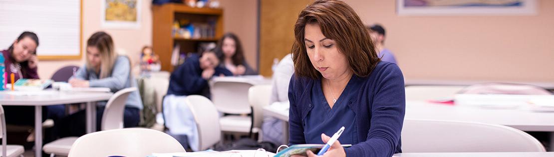 A student raises her hand in a Pima classroom with students interacting with each other